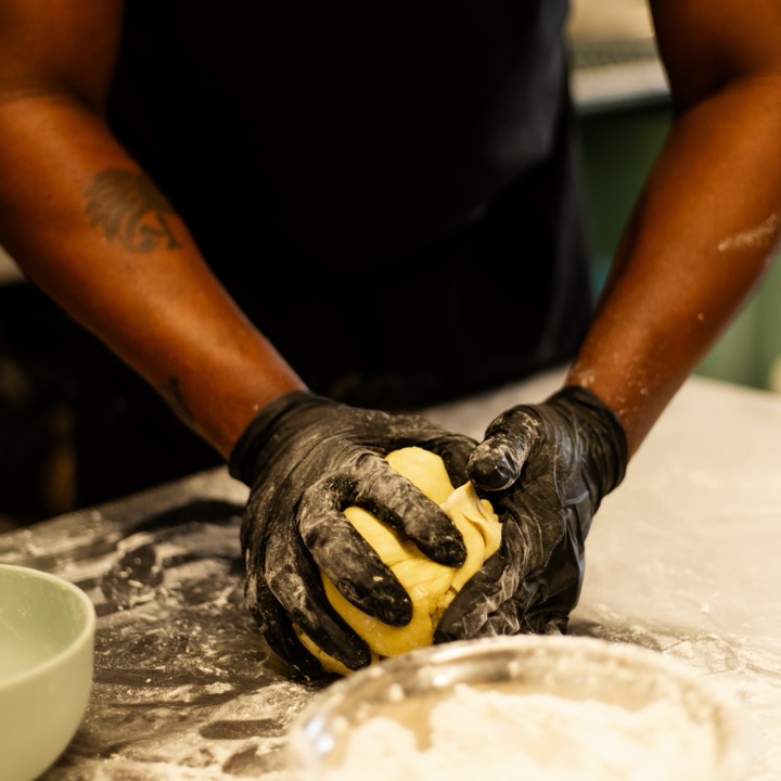 Gloved hands kneading a ball of golden pattie dough